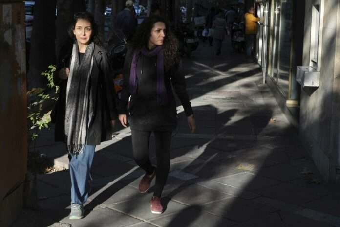 Two Iranian women walk on a sidewalk without wearing their mandatory Islamic headscarves